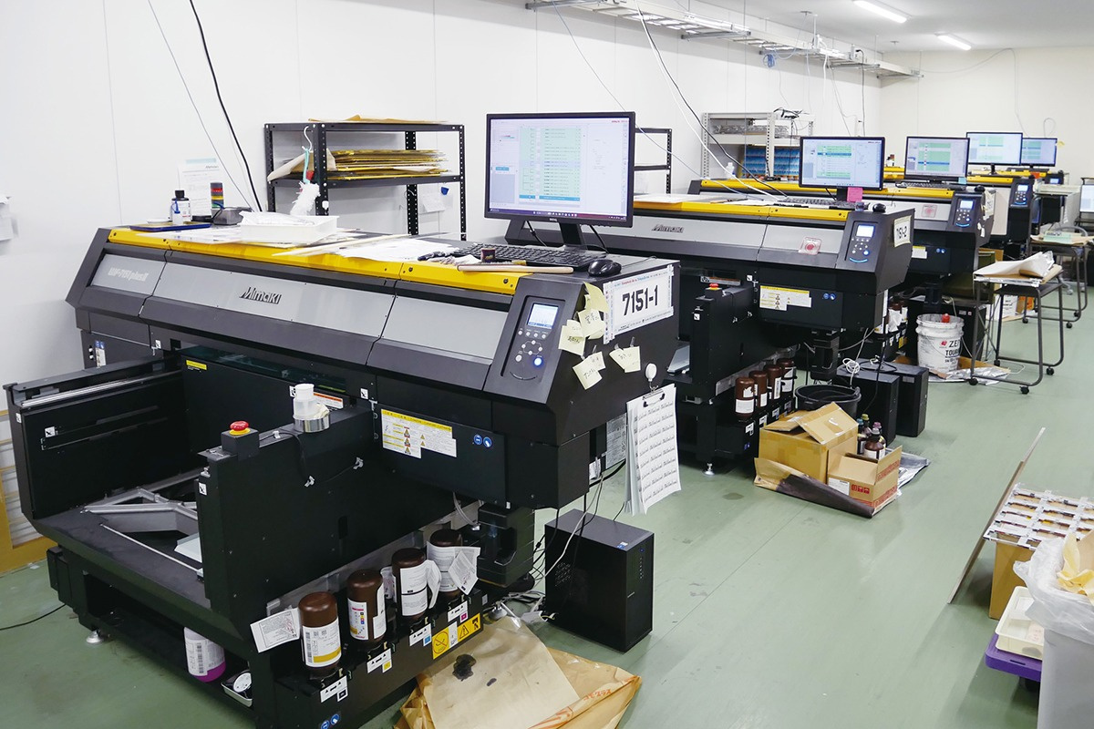 The UJF-6042 flatbed UV printer, first introduced in 2010, has long been used to print acrylic stands and keychains, with monthly production now stable at around 300,000 to 400,000 units. By adopting flexible inks in addition to rigid inks, Idea has also expanded into printing original figurines, smartphone cases, and other items. As of December 2025, a total of 10 printers are installed at the Nagano factory, including four UJF-7151 plusII units. The factory is also equipped with a DCF-605PU digital coating machine.